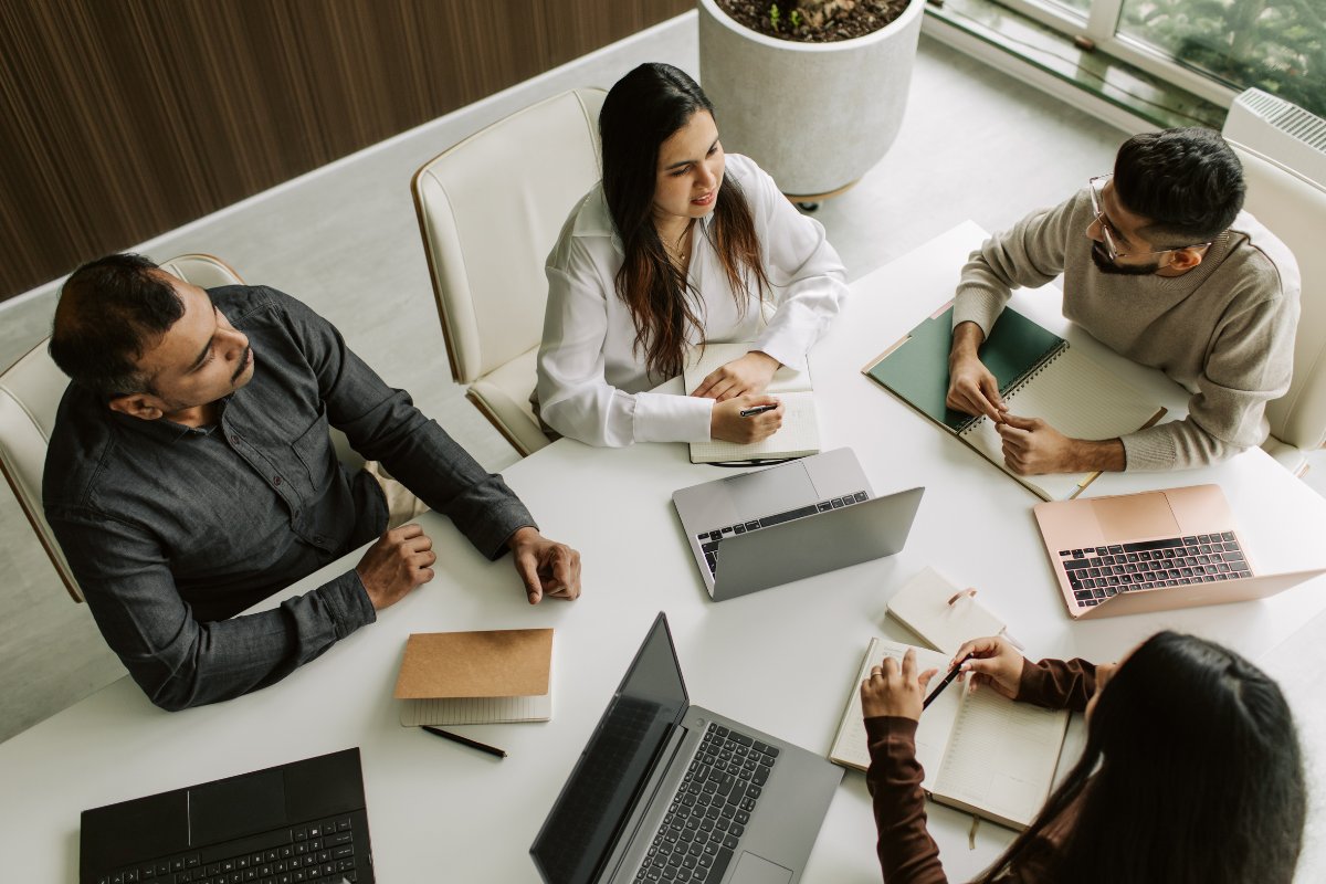 A team meeting around a table with laptops and notebooks